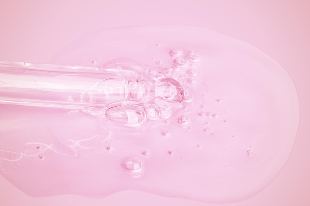 A flowing clear gel from a pipette A lot of flowing gel in a big drop With bubbles On a pink background