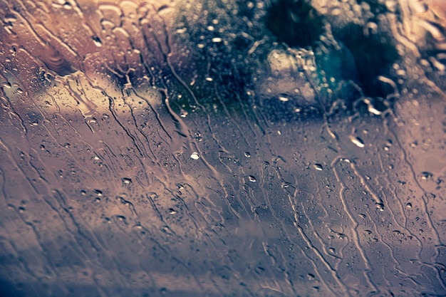 車のフロントガラスの背景に雨のしずくを流れる