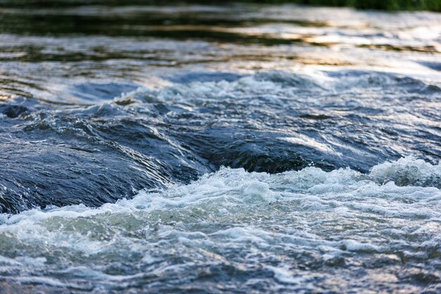 Photo flowing water of a summer river with a small rapid waterfall at evening light