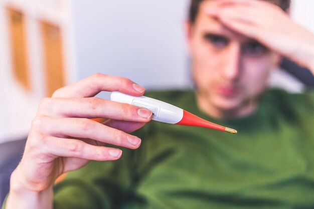 Flu and corona concept Man is holding a fever thermometer in his hand close up