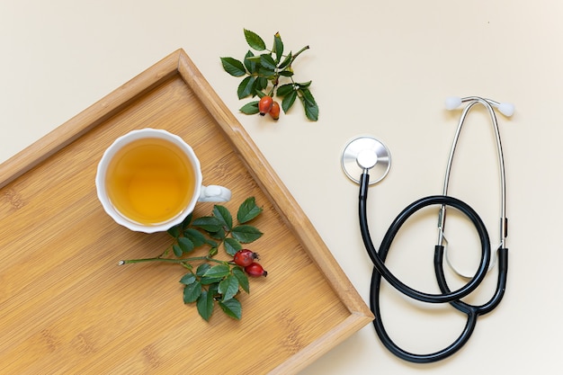 Flu season concept. Cup of herbal vitamin tea on the wooden tray and medical stethoscope.