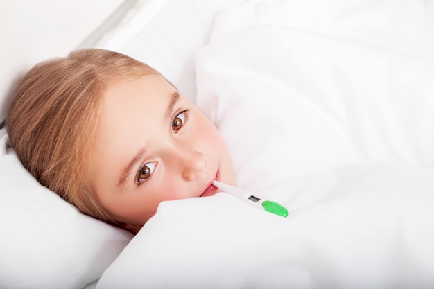 Flu. Young girl lying in bed with a thermometer