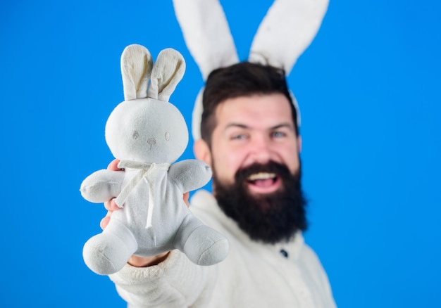 A fluffy pet Bearded man in easter rabbit costume with hare toy Easter rabbit is a symbol of Easter and spring season Happy hipster with long rabbit ears holding bunny toy Fertility and new life