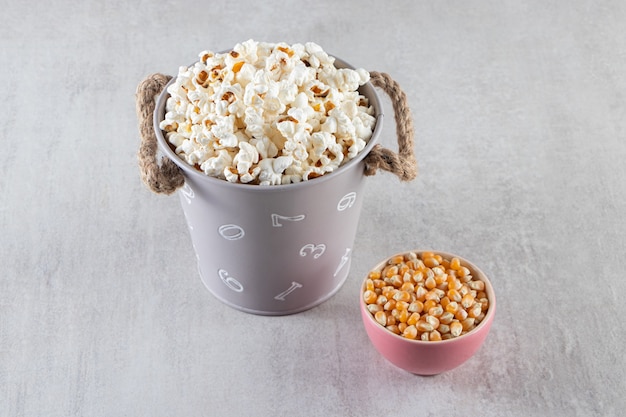 Fluffy popcorn and raw corn kernels on stone background. 