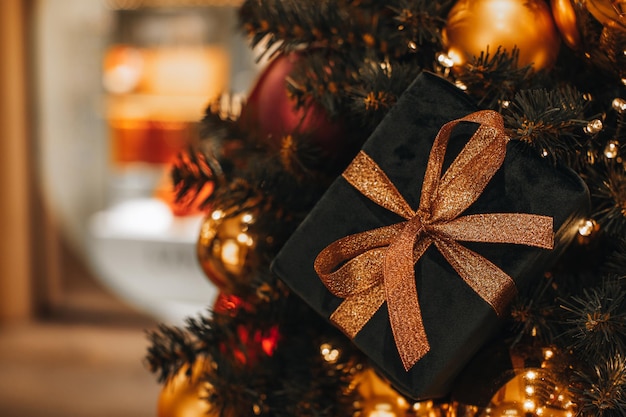 Fluwelen nieuwjaarscadeau met een gouden lint aan de kerstboom Defocused slingerverlichting