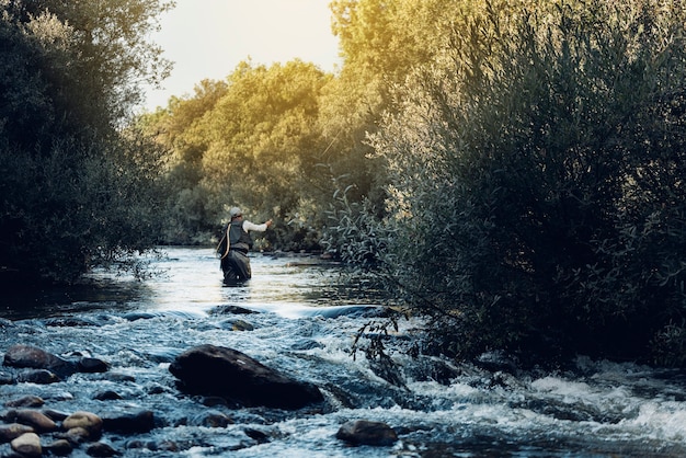 Рыбак нахлыстом, используя удочку в красивой реке.