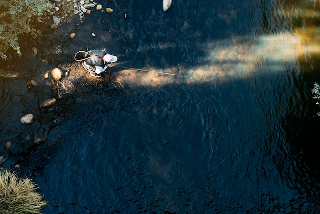 Рыбак нахлыстом, используя удочку в красивой реке.