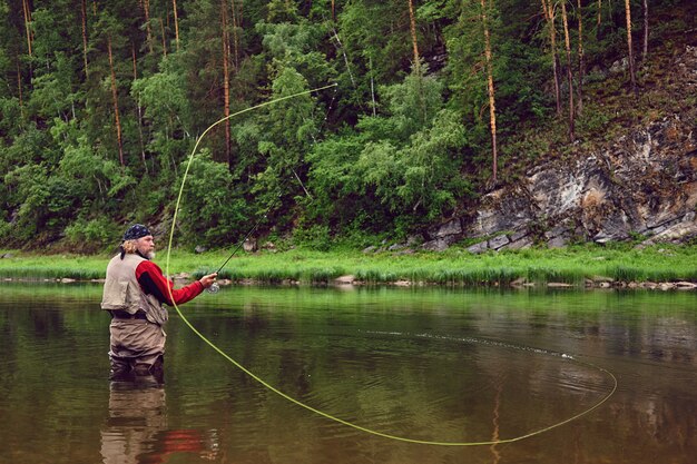 Рыболов нахлыстом делает бросок, стоя в воде