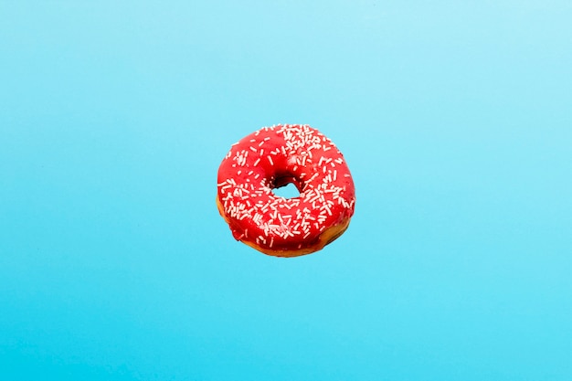 Flying in air donut with red icing on a blue. Bakery, baking concept.