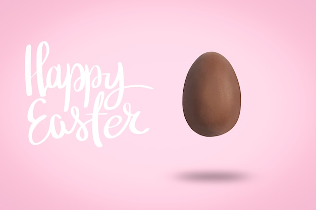 Flying Chocolate Egg on a pink background with the text Happy Easter. Easter concept. Levitation. Flat lay, top view.