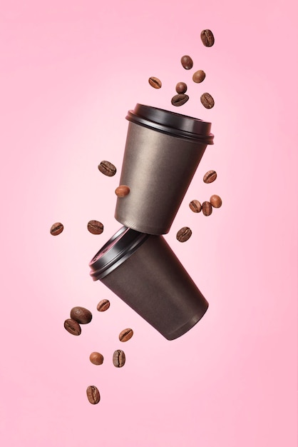 Photo flying coffee from a paper cups with flying coffee beans on a pink background. coffee concept. mock up. empty polystyrene coffee drinking mug mockup front view. clear plain tea take away package.