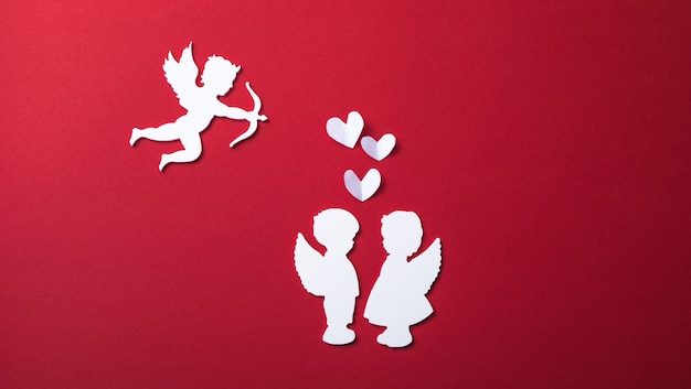Летающий силуэт купидона, два белых ангела, счастливые баннеры Дня святого Валентина, стиль бумажного искусства. Амур на красной бумаге