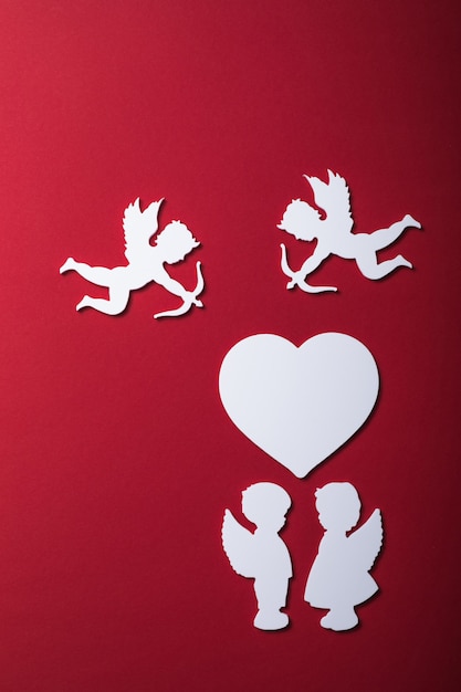 ハート、ギフト、幸せなバレンタインデーのバナー、ペーパーアートスタイルの空飛ぶキューピッドシルエット。赤い紙に情事