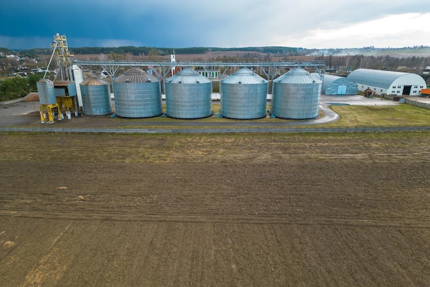 Flying a drone over silver silos on agro manufacturing plant for processing drying cleaning and storage of agricultural products flour cereals and grain Large iron barrels of grain aerial view