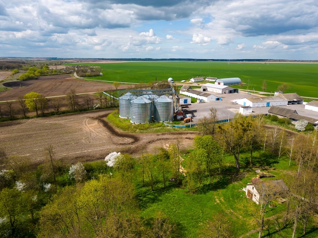Flying a drone over silver silos on agro manufacturing plant for processing drying cleaning and storage of agricultural products flour cereals and grain Large iron barrels of grain aerial view