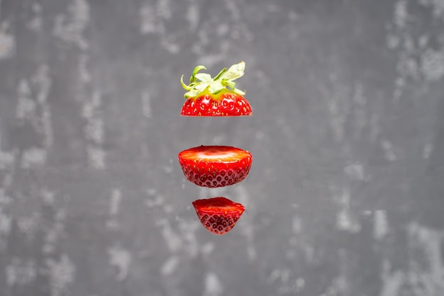 Flying fresh delicious ripe red strawberry cut into slices\
isolated on concrete background. food levitation concept.