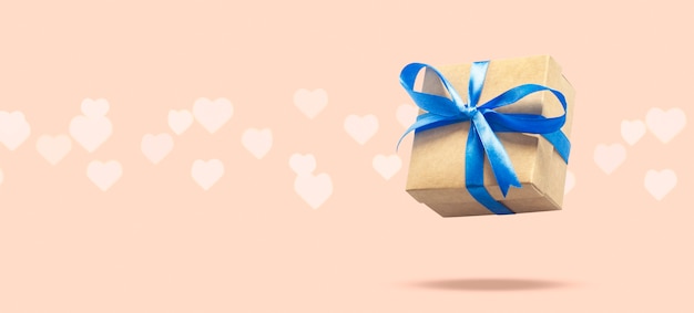 Подарочная коробка летая на светло-розовой поверхности с боке в форме сердца. Концепция праздника, подарок, продажа, свадьба и день рождения.