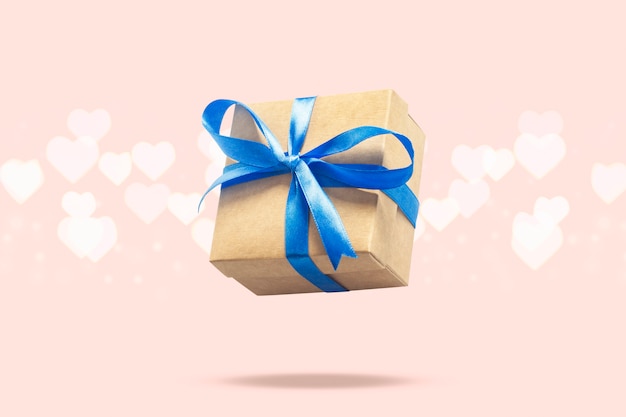 Flying gift box on a light pink surface with heart shaped bokeh. Holiday concept, gift, sale, wedding and birthday.