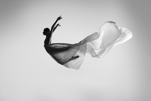 Foto volare in alto ballo di danza professionale con velo trasparente che fa movimenti in un salto in bianco e nero