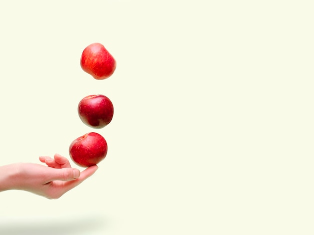 Flying levitating floating red ripe fresh juicy apples in air above female womens hand on green background Levity summer fruits Trendy minimal Creative food