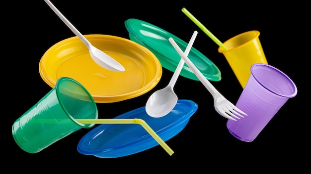 Flying multicolored disposable plastic tableware on a black background The concept of ecology and