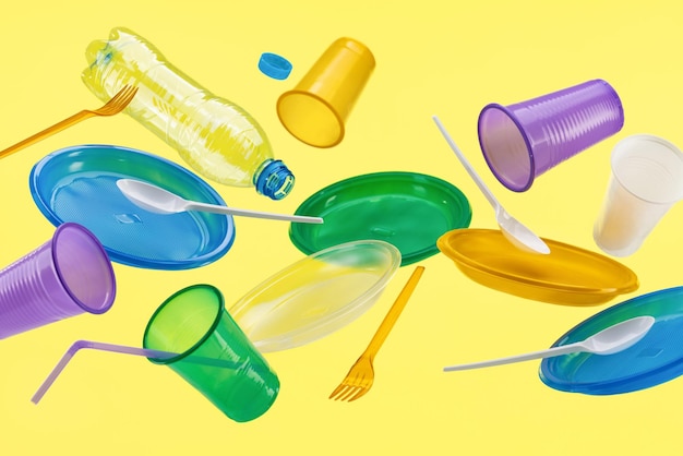 Flying multicolored plastic utensils on a yellow background Environmental protection