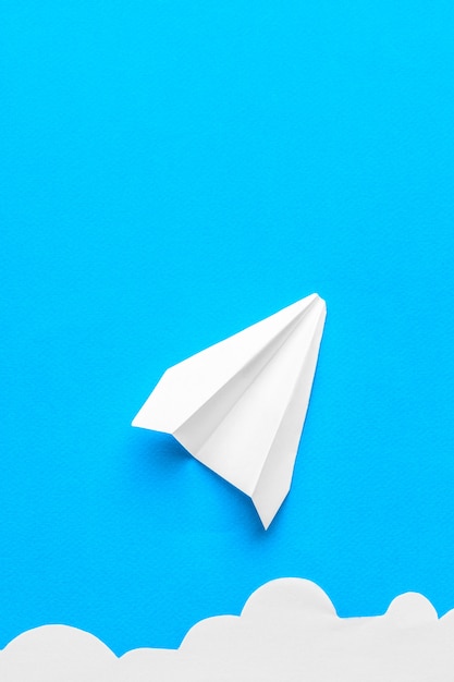 Photo flying paper plane in the clouds on a blue background. concept of flight, travel, transfer