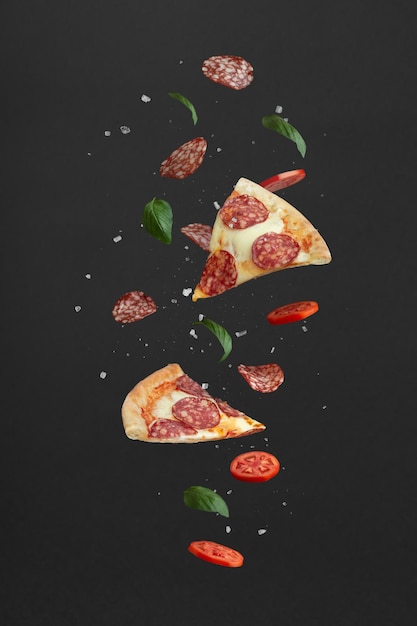 Foto pezzi di pizza e ingredienti volanti su sfondo nero