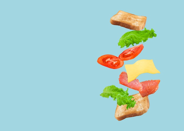 Photo flying sandwich with salmon, cheese and tomatoes on a blue.