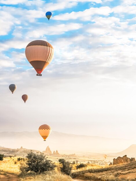 Foto volando nel cielo molti bellissimi palloncini di colori brillanti in aria in cappadocia nelle montagne all'alba del sole riempiendo il palloncino con aria calda dal bruciatore grande cestino turisti escursione volo nuvola