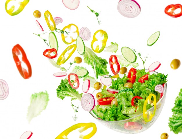 Flying vegetable salad ingredients over transparent bowl. Vitamins and healthy eating concept.