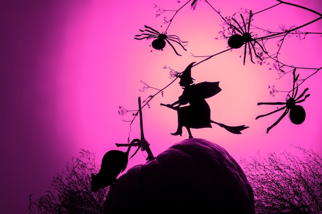 A flying witch silhouette and spiders of black paper on pink gradient