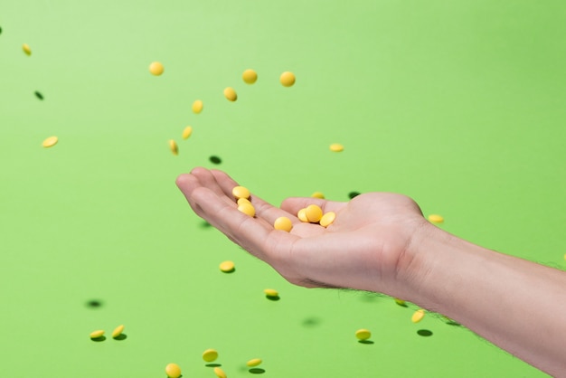 Flying yellow pills from hand in front of green background