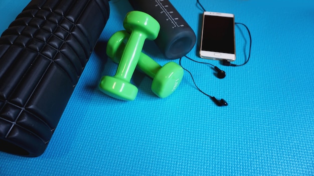 Foam Roller met groene dumbbells en waterfles en telefoon met koptelefoon - Gym Fitness Equipment Blauwe achtergrond zelf Myofascial Release - MFR.