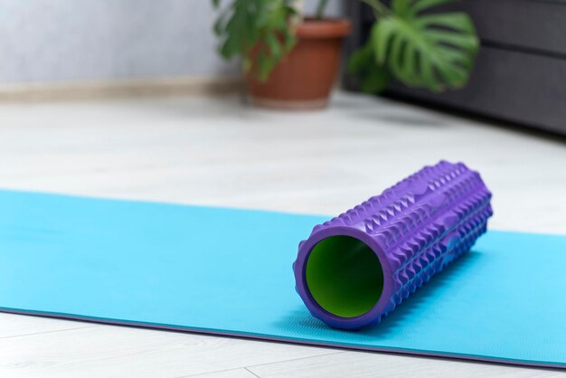 Foam roller for self-massage on blue yoga mat. Equipment for myofascial release. Massage roller. MFR.