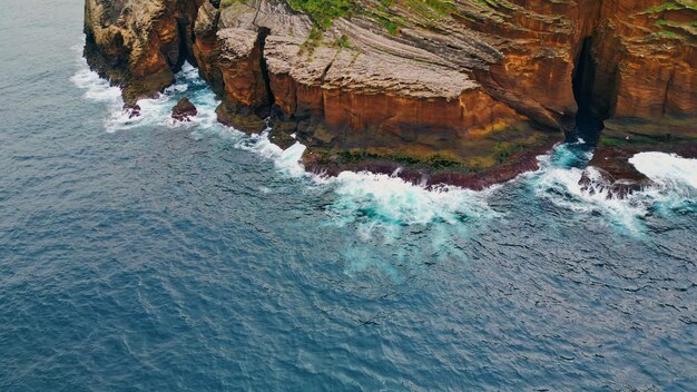 Foaming waves crashing rocky coastline aerial wild sea washing reef rock cliffs