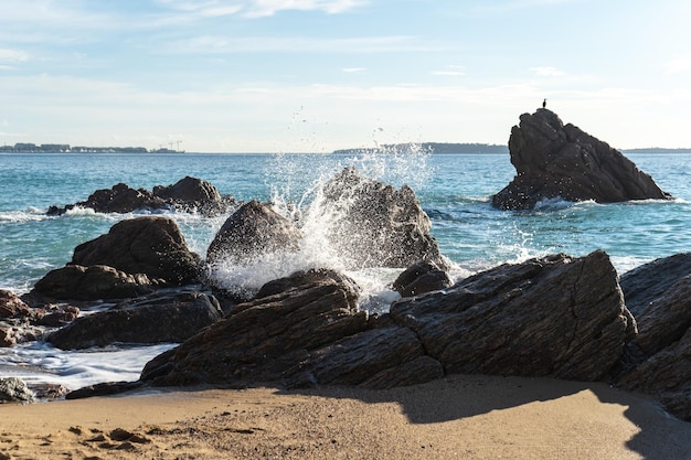 写真 岩の多いビーチのテクスチャ背景に泡立つ海の波の嵐青い海水岩海岸パターン
