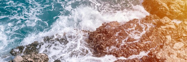 Foamy waves of clear blue sea water beat against the rocky shore of the ocean banner flare