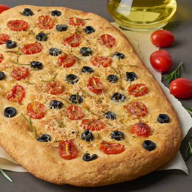Focaccia, pizza, italian flat bread with tomatoes, olives and rosemary on brown table