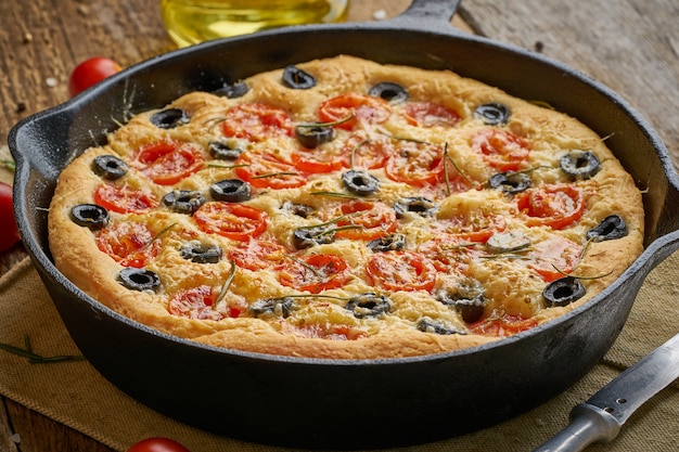 Focaccia, pizza in skillet. Close up italian flat bread with tomatoes, olives and rosemary