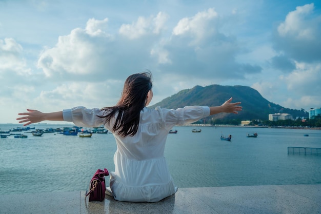 Vung Tau Travel 컨셉트에서 행복한 아시아 소녀가 해변 앞에서 손을 들어올리는 모습에 초점을 맞춥니다