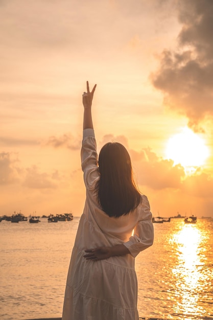 Vung Tau Travel 컨셉트에서 행복한 아시아 소녀가 해변 앞에서 손을 들어올리는 모습에 초점을 맞춥니다