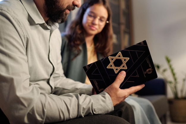 Photo focus on black cover of torah with star of david in hands of bearded rabbi