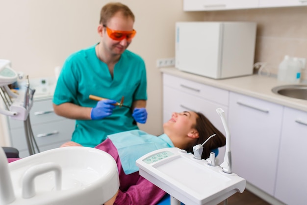 Focus on closeup of dental equipment holder including instruments and jaw model Smiling teenage female is sitting in chair and waiting for treatment