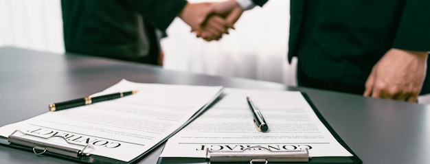 Focus closeup panorama business contract paper with pen while two professionals shake hand in blurred background signifying successful negotiation and partnership agreement with handshaking Prodigy