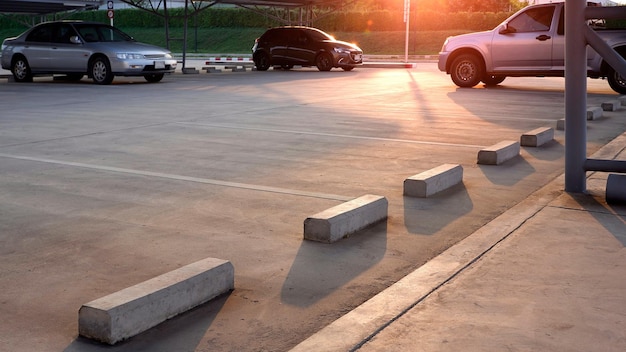 Focus at concrete wheel stops with empty space and three cars parked in outdoor parking lot area