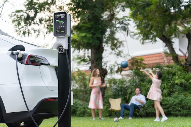 Photo focus electric vehicle recharge from home charging station on blur background of happy and playful family playing together ev car using alternative and sustainable energy for better futuresynchronos