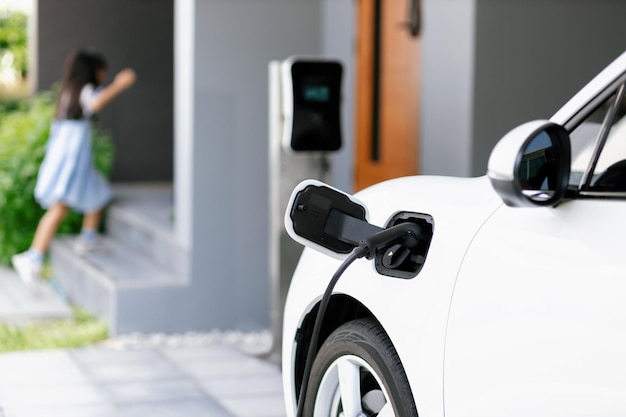 ぼかした女の子を背景に、自宅の充電ステーションで EV 車を充電することに焦点を当てる
