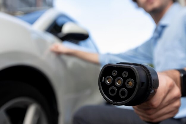 Focus EV charger plug pointing at camera with blur progressive man in background