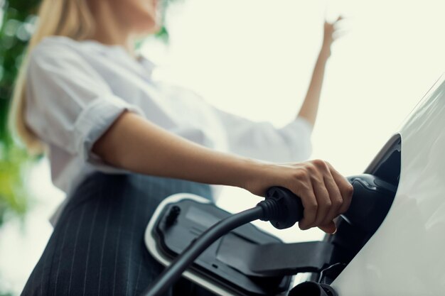 Вилка зарядного устройства Focus EV с размытой прогрессивной женщиной, заряжающей электромобиль на заднем плане